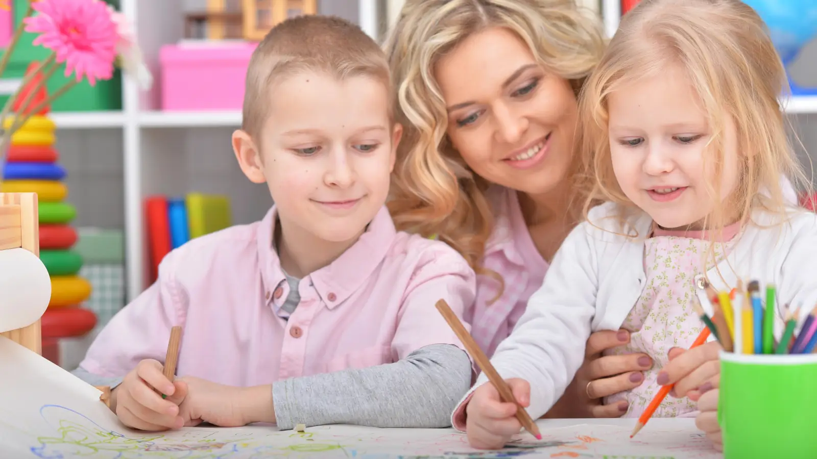 Toddler quietly colouring in a square activity book at the kitchen table while a parent relaxes with a coffee in the background